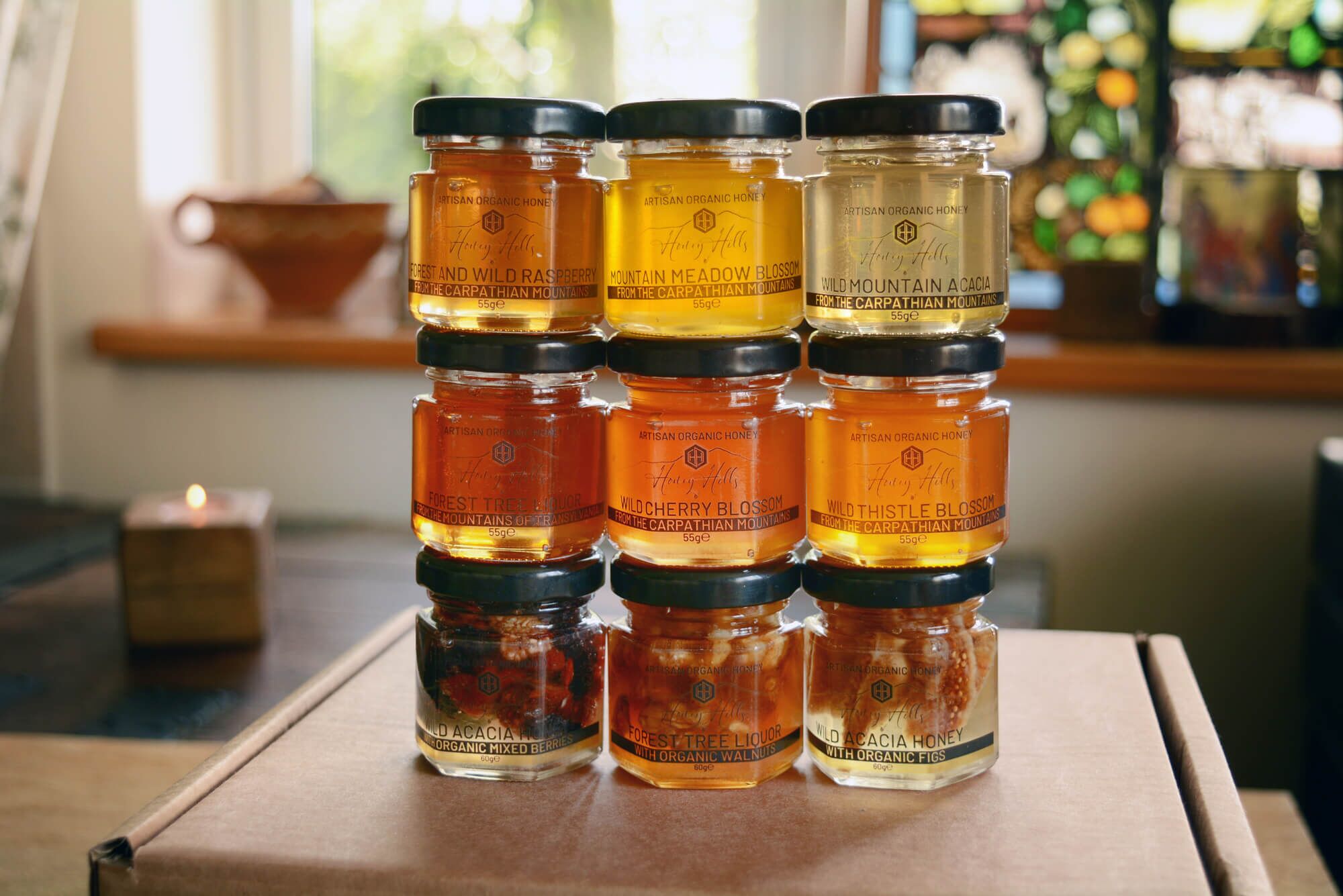 hamper-box-taster-set-honey-inclusions - Honey Hills - Online artisan shop with delicious, rare raw mountain honey varieties Colourful selection of artisanal organic honey jars stacked on a wooden surface, showcasing various floral flavours and textures.