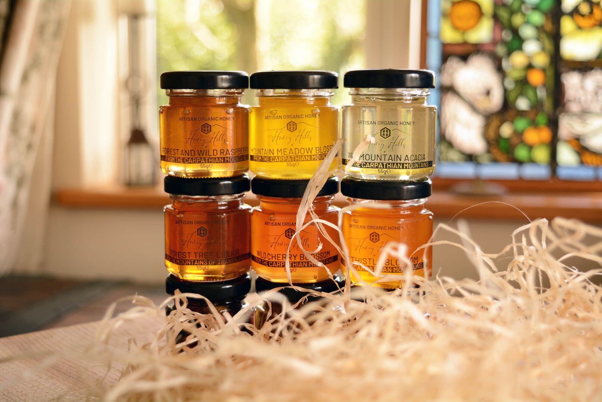 hamper-box-taster-set-honey - Honey Hills - Online artisan shop with delicious, rare raw mountain honey varieties Selection of artisan organic honey jars, showcasing various flavours against a cozy background with natural light.