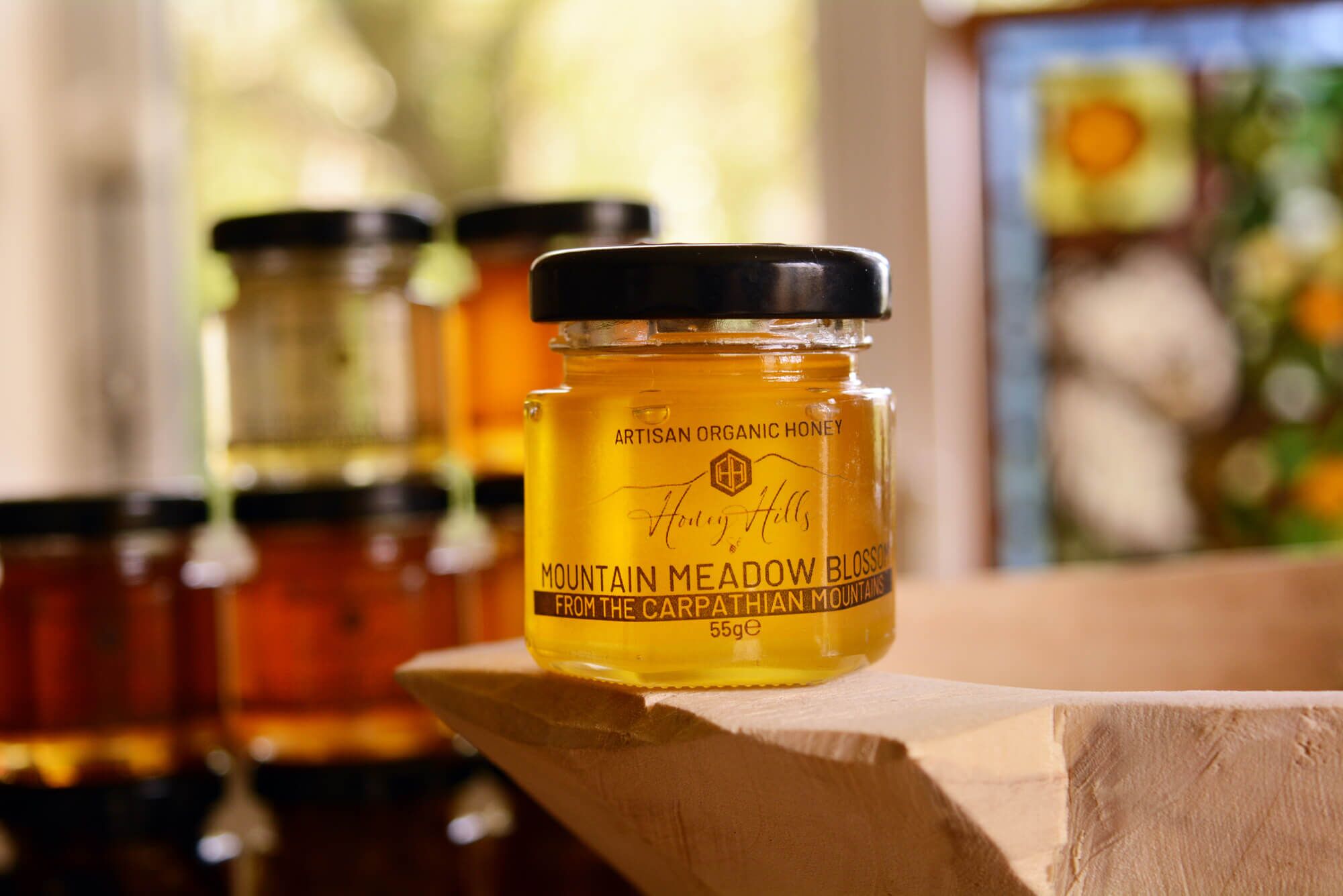 hamper-box-taster-set=mountain-meadow-honey - Honey Hills - Online artisan shop with delicious, rare raw mountain honey varieties Artisan organic honey jar labeled “Mountain Meadow Blossom” from the Carpathian Mountains, sitting on a wooden bowl.