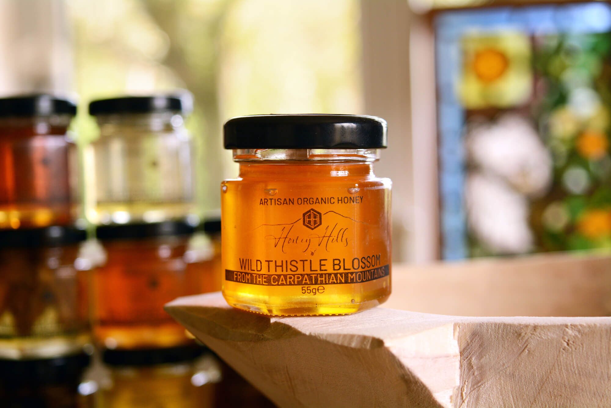 hamper-box-taster-set-thistle-honey - Honey Hills - Online artisan shop with delicious, rare raw mountain honey varieties Artisan organic wild thistle blossom honey in a glass jar on a wooden surface, highlighting natural ingredients and craftsmanship.