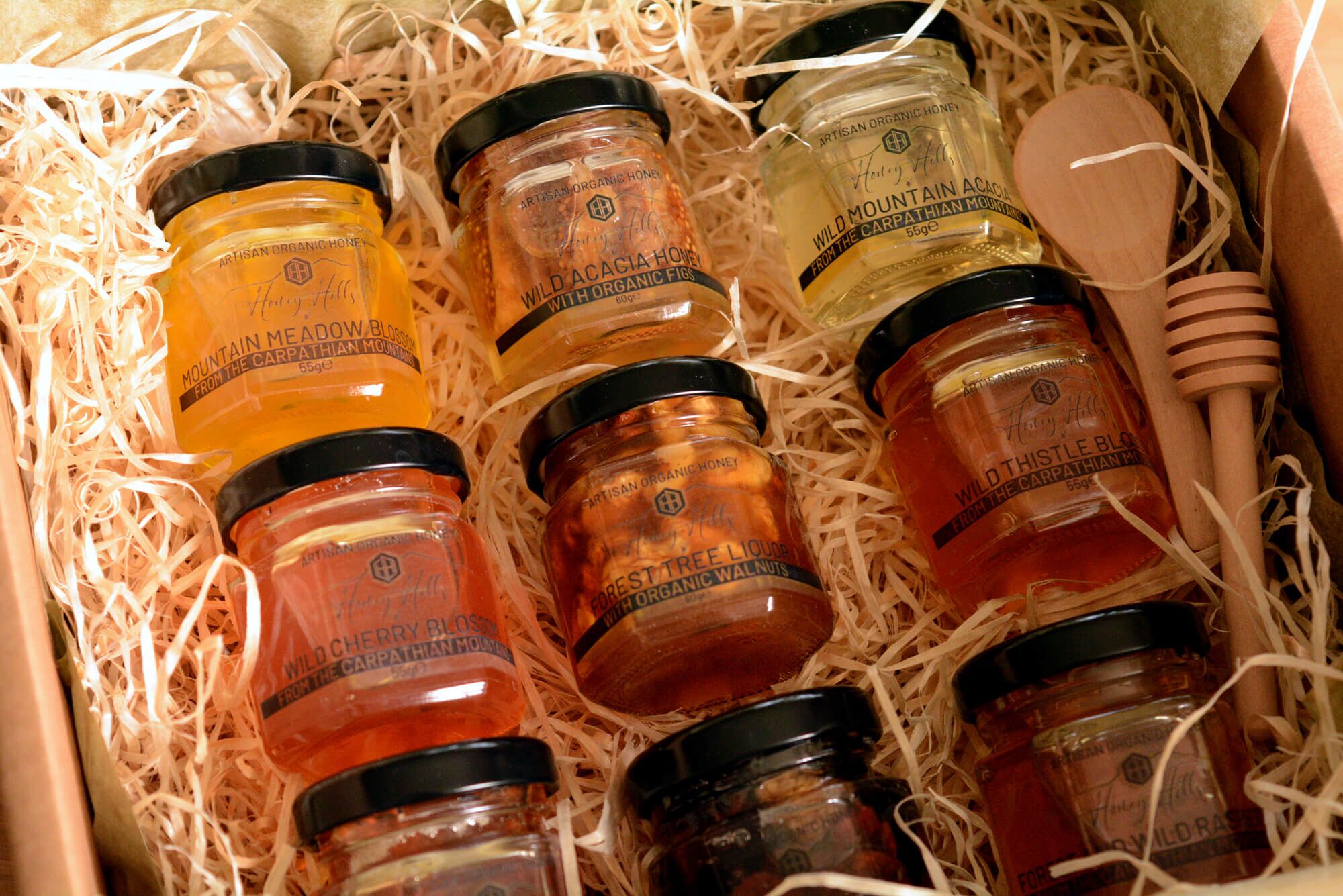hamper-box-honey-taster-set - Honey Hills - Online artisan shop with delicious, rare raw mountain honey varieties Collection of artisanal honey jars in a gift box, showcasing various flavours and organic labels, perfect for sweet gifts.